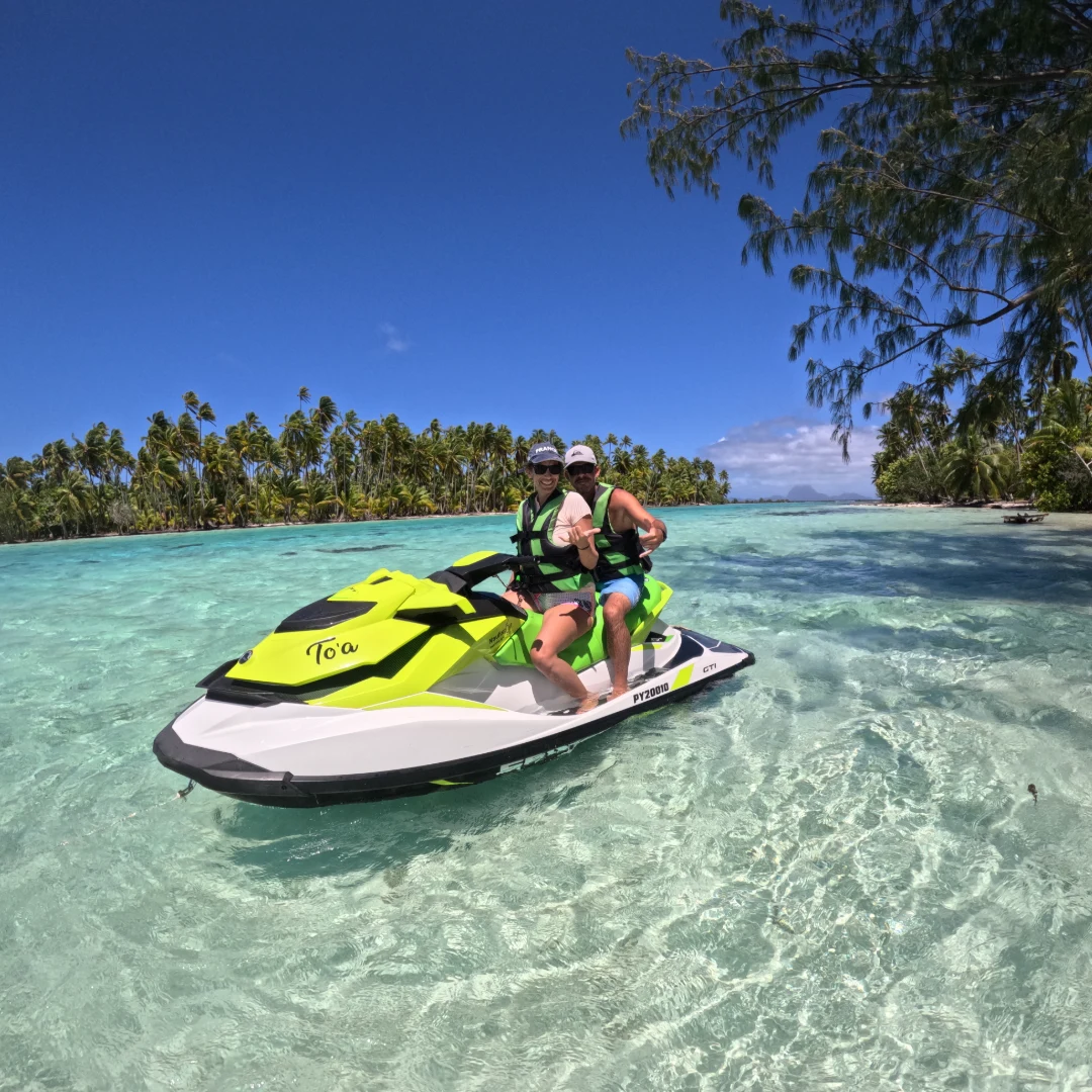 Couple sur un jet ski nommé "To'a" dans l'eau cristalline près d'un rivage bordé de palmiers à Raiatea. Couple près d'une plage de palmiers